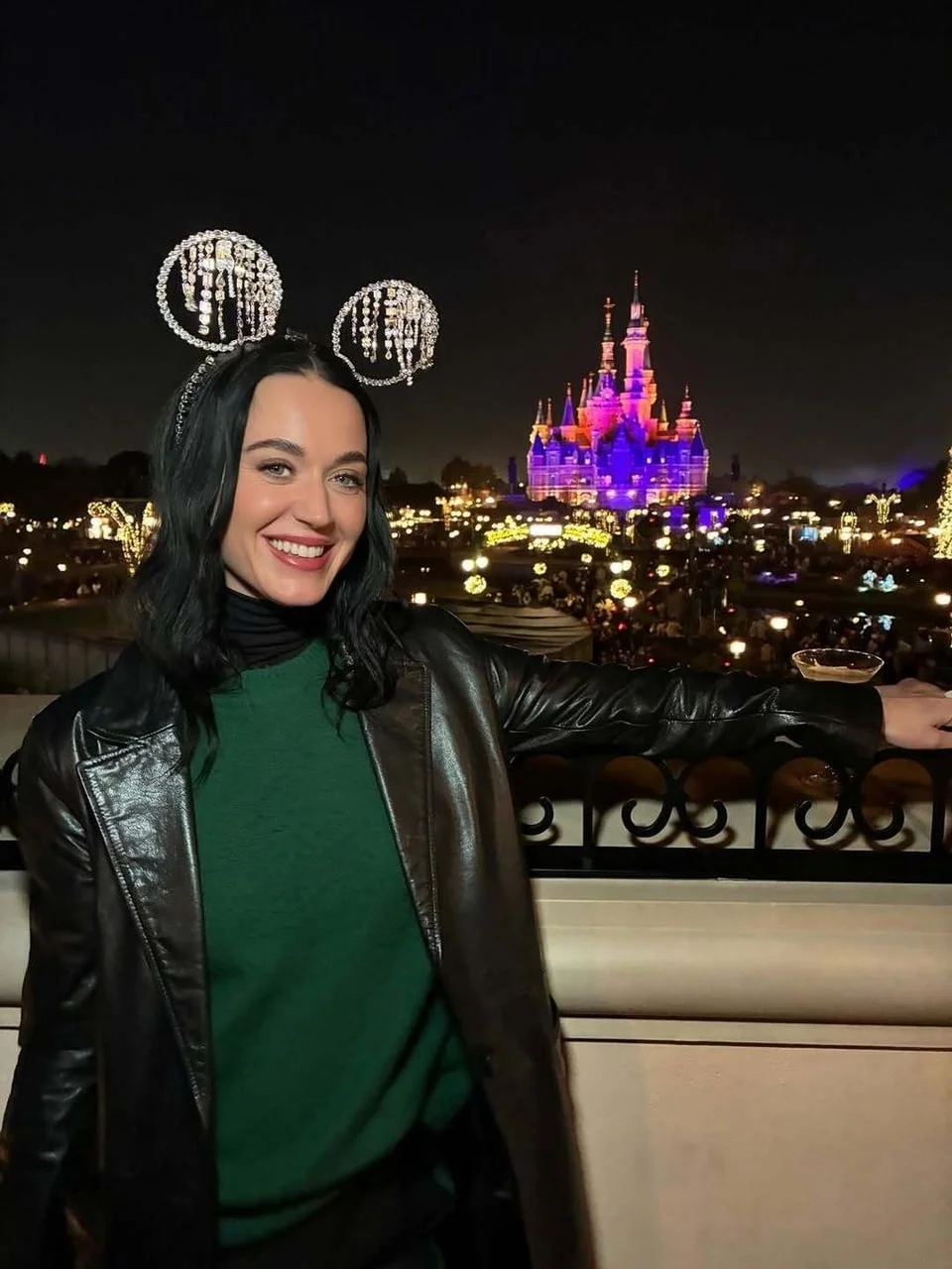 Katy Perry nosi svjetlucave uši Mickeyja Mousea ispred osvijetljenog dvorca noću.