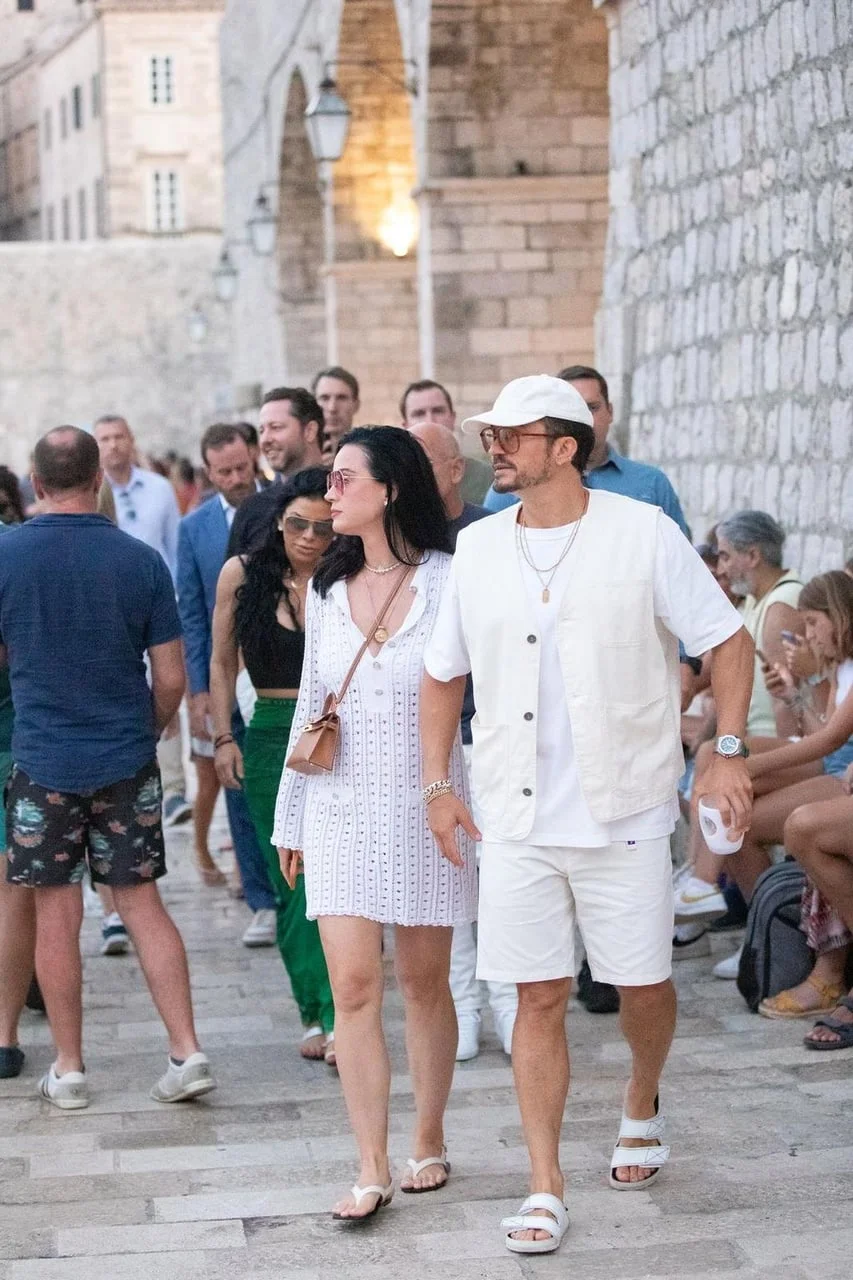 Katy Perry i Orlando Bloom šeću povijesnom kamenom ulicom u bijeloj ljetnoj odjeći.