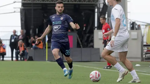 Nogometaš u tamnom dresu s brojem 39 vodi loptu na travnjaku tijekom utakmice.