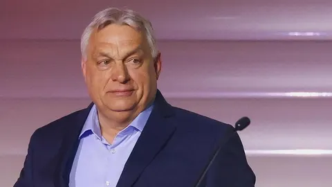 Viktor Orbán u tamnoplavom odijelu i svijetlo plavoj košulji stoji za govornicom.