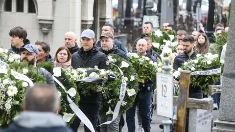 Ljudi u pogrebnoj povorci nose vijence s bijelim cvijećem na beogradskom groblju.
