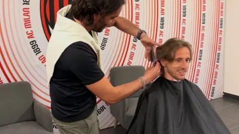 Luka Modrić sjedi kod frizera dok mu on uređuje kosu škarama.