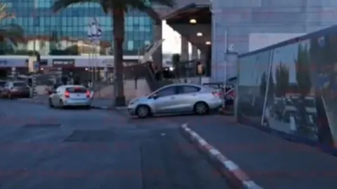 Srebrni automobil parkiran na ulici ispred moderne poslovne zgrade s palmom.