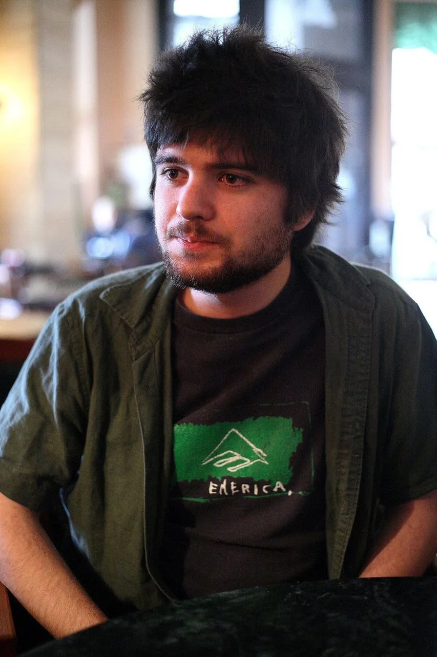 Mladi Filip Riđički sjedi u kafiću u tamnoj majici i zelenoj košulji.