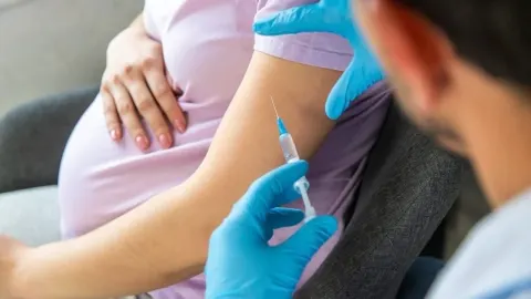 Liječnik u plavim rukavicama daje cjepivo u nadlakticu trudnice.