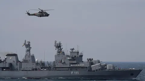 Vojni brod s oznakom F 111 i vojni helikopter u letu iznad otvorenog mora.