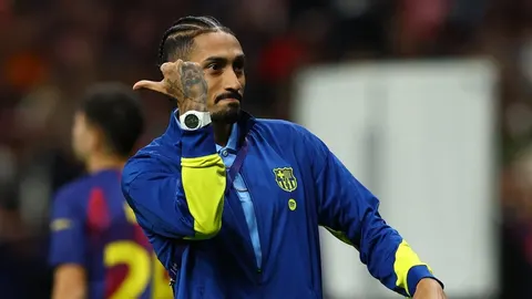 Raphinha u plavoj trenirci Barcelone s podignutom rukom i ozbiljnim izrazom lica