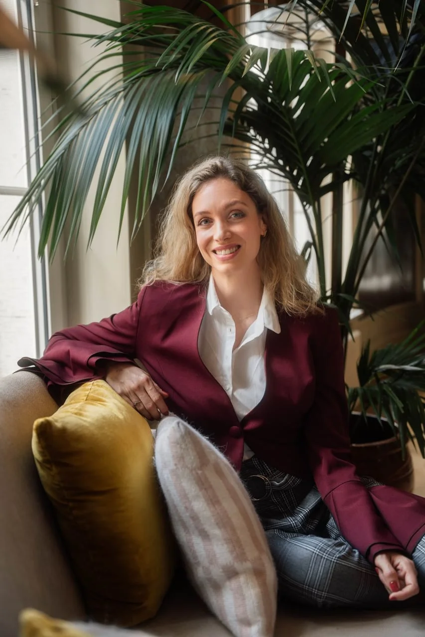 Hana Huljić sjedi na kauču u tamnocrvenom sakou i bijeloj košulji.