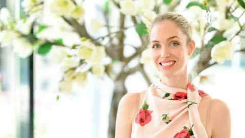 Hana Huljić nasmijana ispred dekorativnog stabla s bijelim cvjetovima.