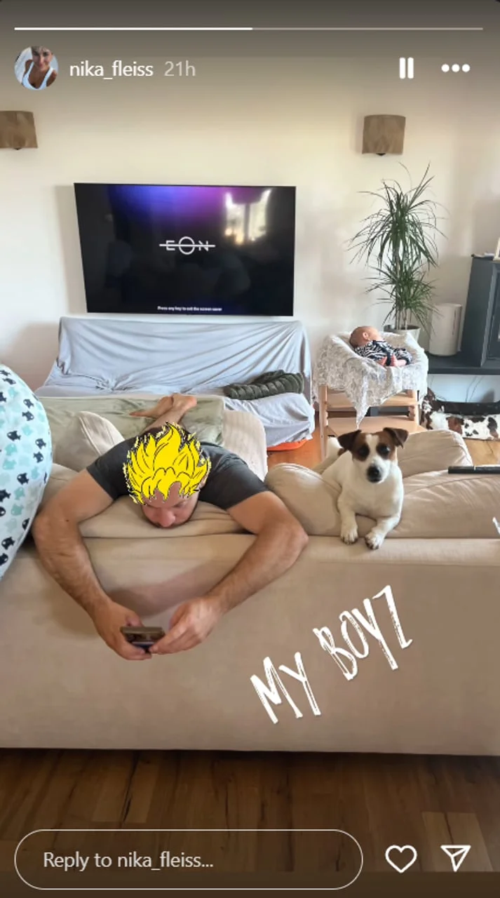 Muškarac leži na kauču s mobitelom, dok beba spava u pozadini.