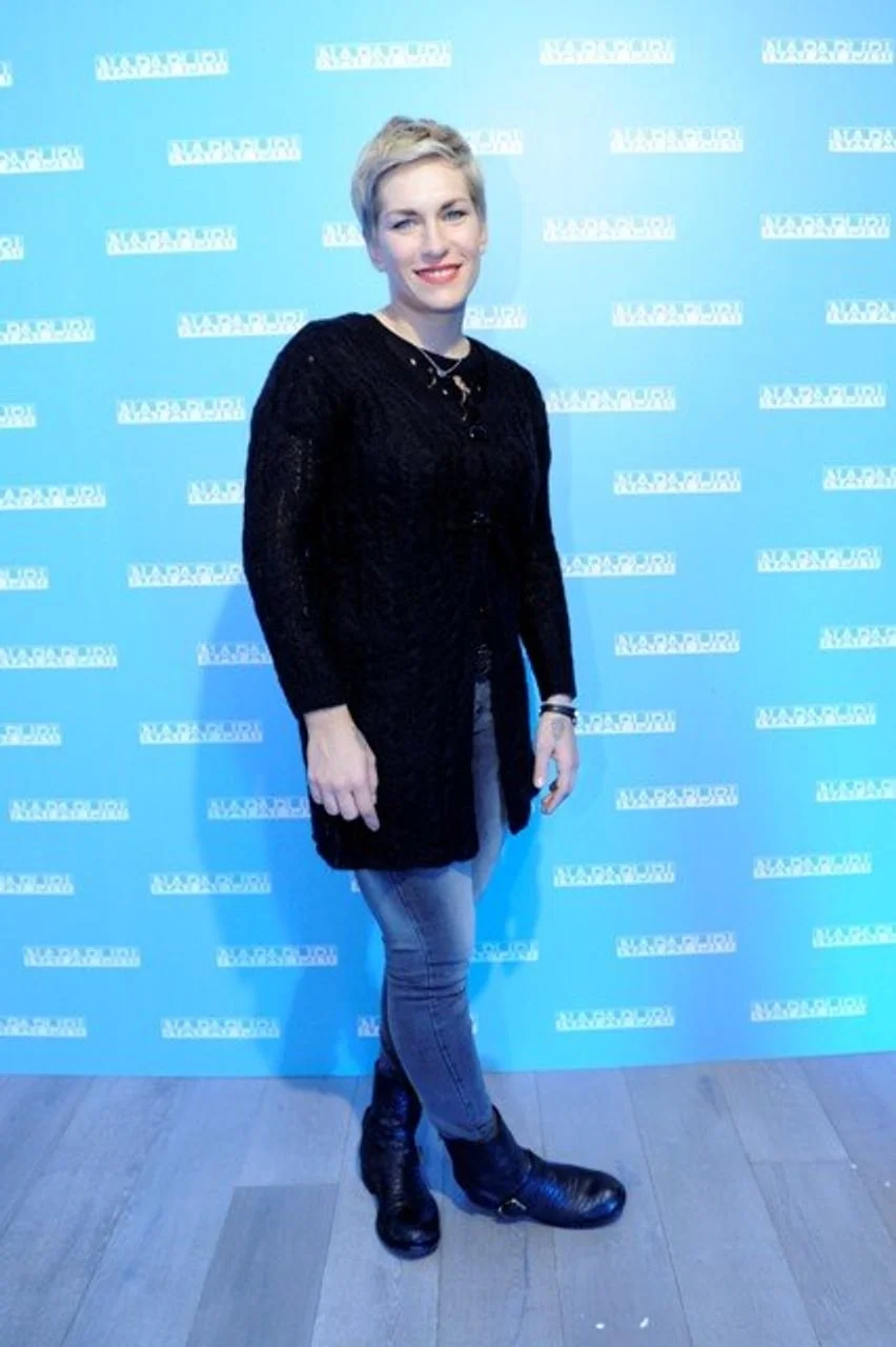 Nika Fleiss u crnoj vesti i trapericama pozira ispred plavog zida.