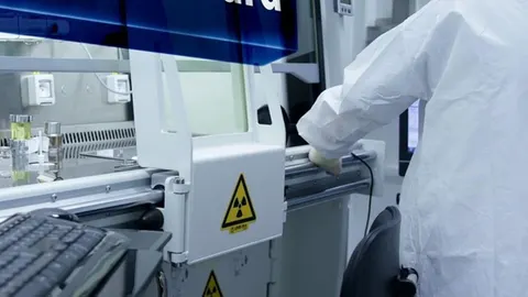 Znanstvenik u bijelom zaštitnom odijelu radi u laboratoriju s opremom pod tlakom.