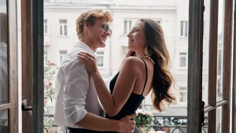 Nasmiješeni par u zagrljaju na balkonu s gradskom pozadinom