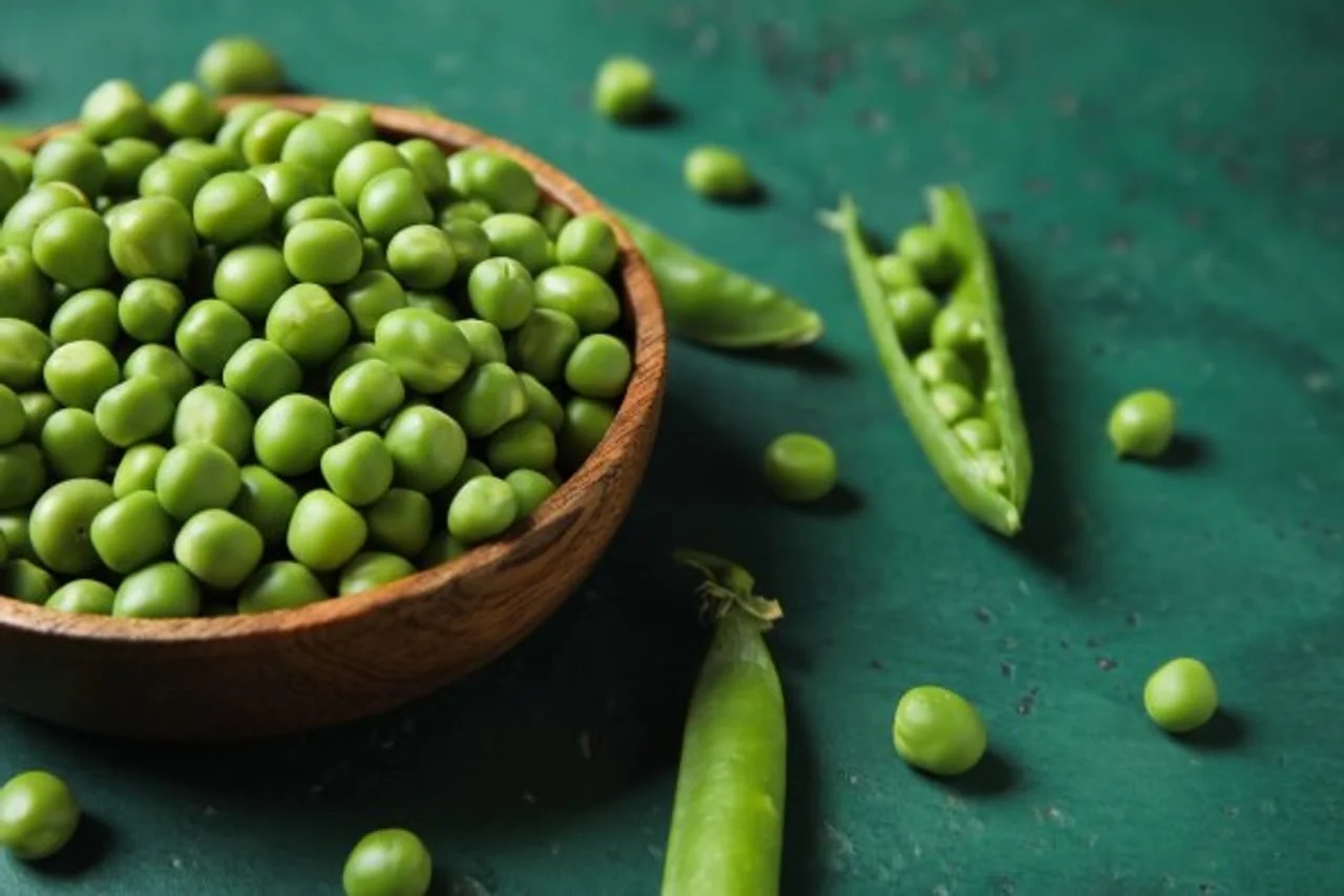 Svježa zrna graška u drvenoj zdjeli na zelenoj površini.