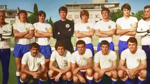 Grupna fotografija nogometaša Hajduka u bijelim dresovima i plavim hlačicama na terenu.