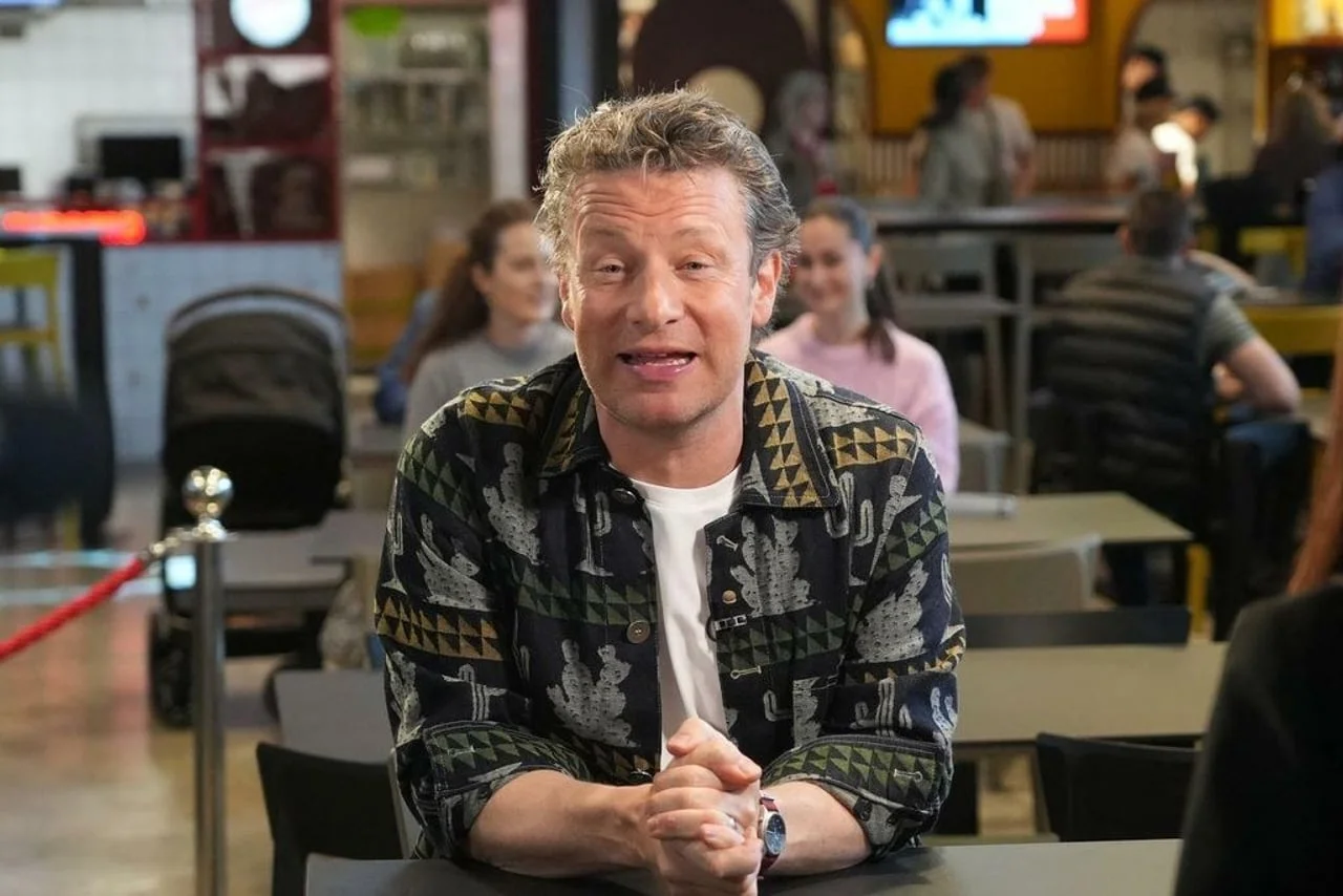 Jamie Oliver u razgovoru s prisutnima u modernom interijeru restorana.