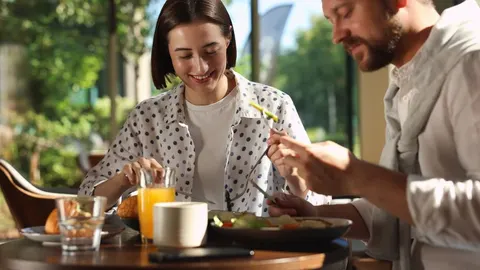 Nasmijani muškarac i žena jedu zdrav doručak uz svježi sok od naranče