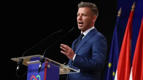 Peter Magyar u plavom odijelu govori za govornicom s mikrofonima