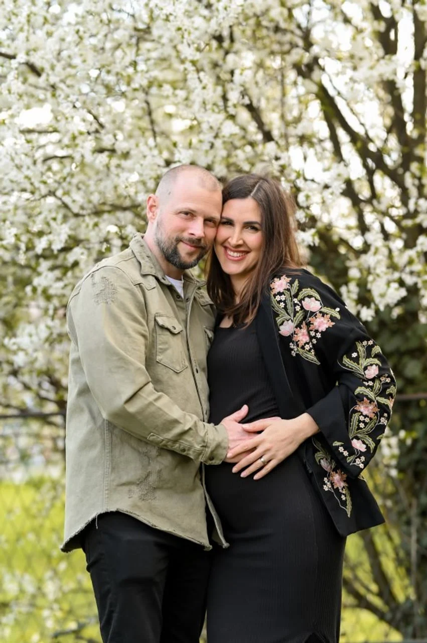 Alan drži ruku na trudničkom trbuhu supruge Ricarde ispred procvjetalog drveta