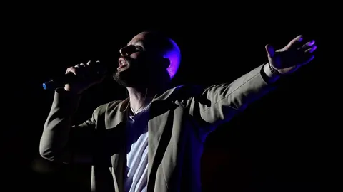 Alan Hržica pjeva na pozornici s mikrofonom i raširenom rukom