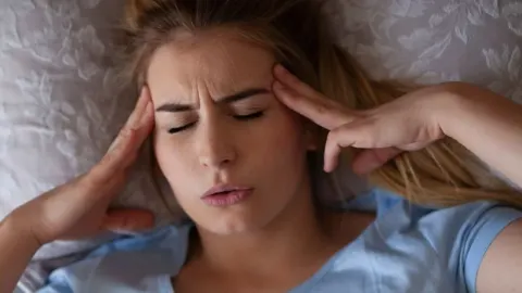 Žena leži i drži se za sljepoočnice zbog bolova u glavi