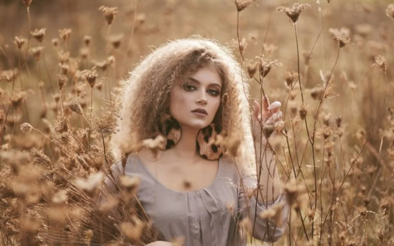 Djevojka s gustom kovrčavom kosom stoji u polju suhog cvijeća.