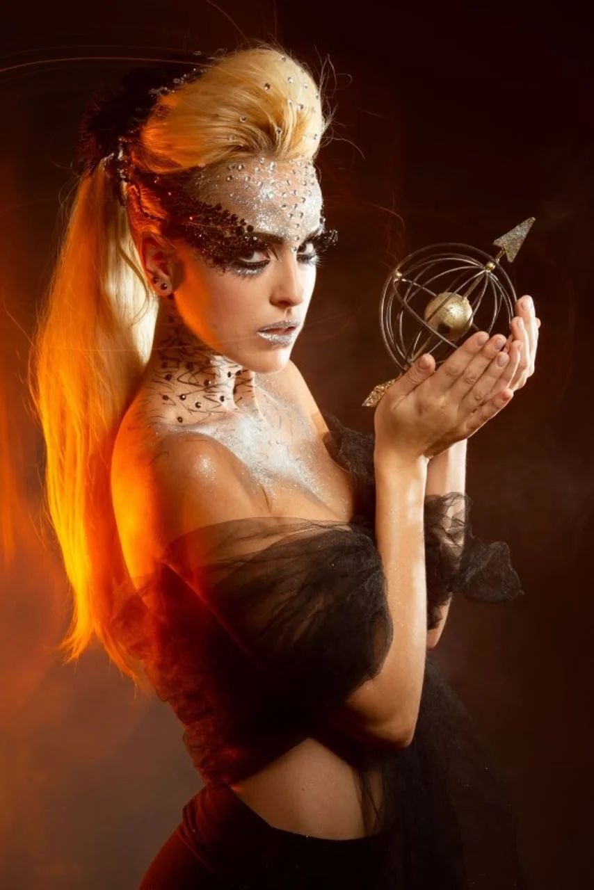 Žena s dramatičnom šminkom drži metalni model nebeske sfere.