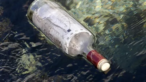 Staklena boca s pismom pluta u plitkoj morskoj vodi