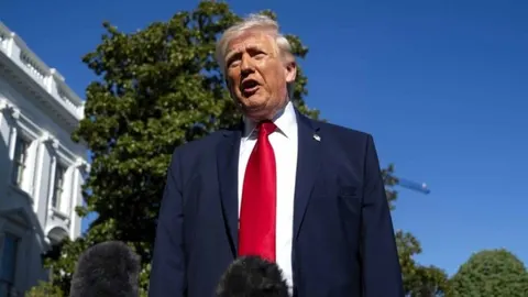 Donald Trump u tamnom odijelu s crvenom kravatom govori ispred Bijele kuće