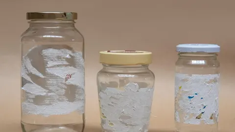 Tri staklene staklenke s ostacima papirnatih naljepnica i ljepila na bež pozadini