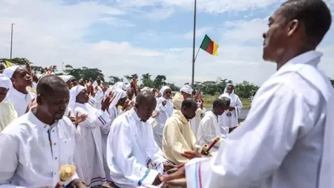 Vjernici u bijelim haljinama pjevaju i mole se na otvorenom u Kamerunu.