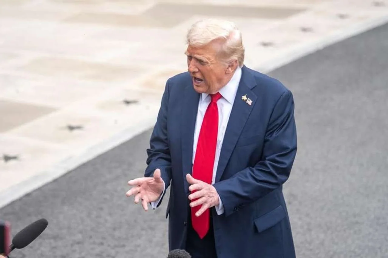 Donald Trump u tamno plavom odijelu s crvenom kravatom govori pred mikrofonima.