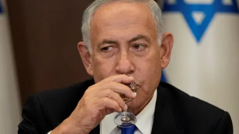 Benjamin Netanyahu u krupnom planu dok pije piće iz male čaše.