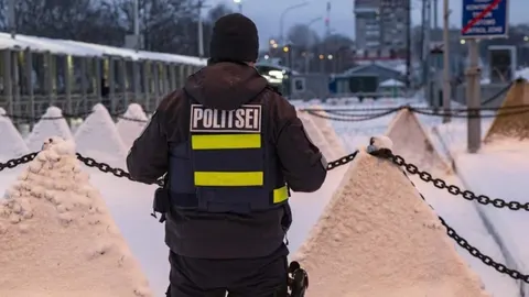 Estonski policajac stoji ispred protutenkovskih prepreka na snijegu.