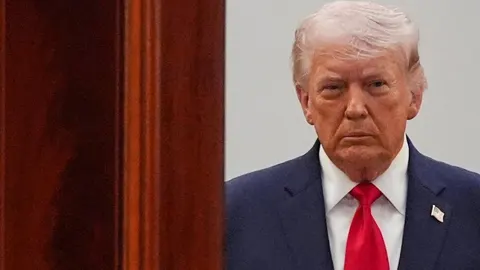 Donald Trump u tamnom odijelu s crvenom kravatom gleda prema naprijed.