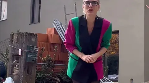 Ida Prester u šarenom sakou ispred nedovršenog gradilišta s ciglama i skelama.