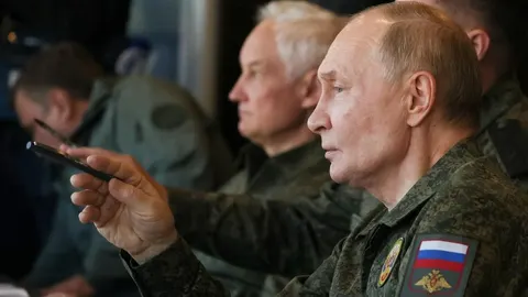 Vladimir Putin u vojnoj uniformi s ruskim obilježjima sjedi na sastanku.