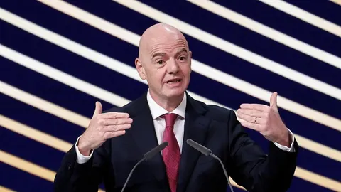 Gianni Infantino govori za govornicom s podignutim rukama.