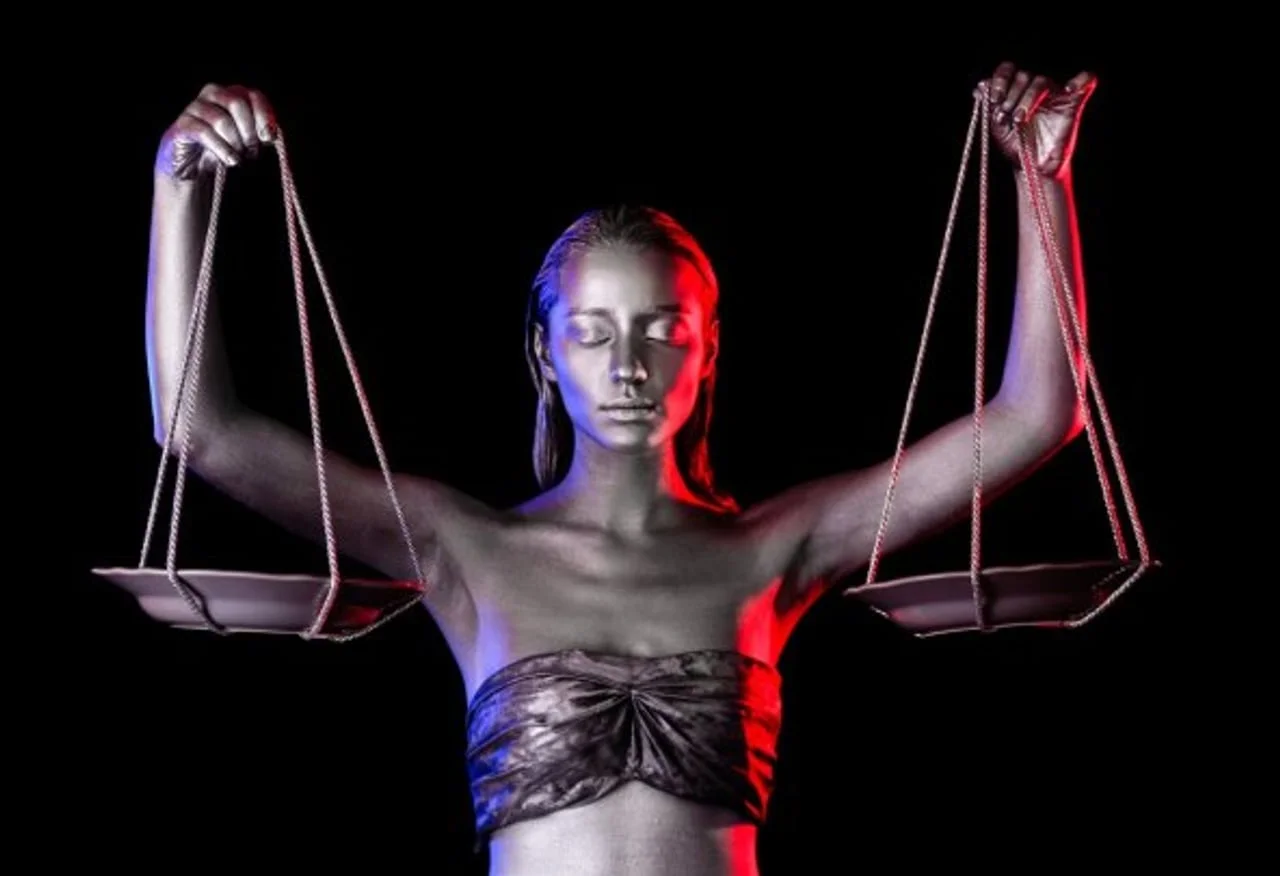 Žena srebrne kože drži vagu u rukama na tamnoj pozadini