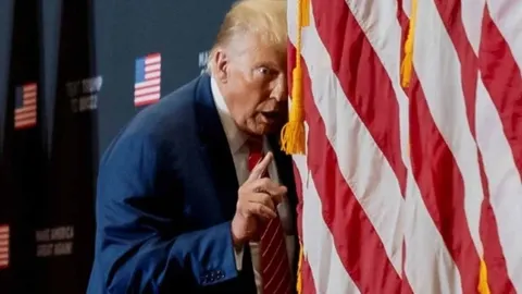 Donald Trump stoji iza američke zastave i podiže kažiprst tijekom govora.