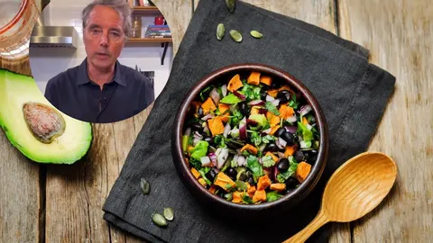 Dan Buettner i zdjela sa salatom od graha, batata i povrća na drvenom stolu.