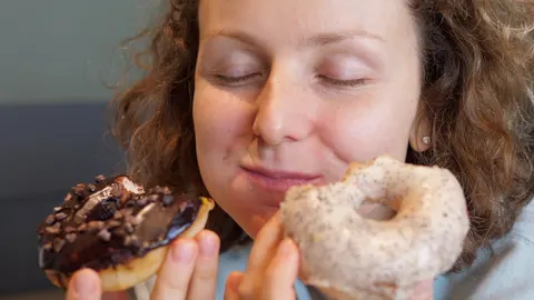 Žena zatvorenih očiju drži čokoladnu krafnu i krafnu sa šećerom.