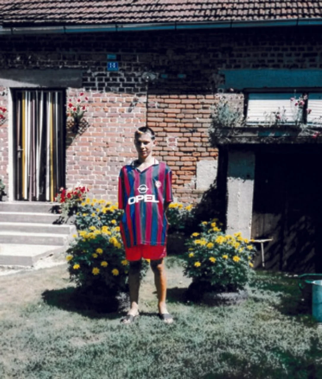 Dječak u prugastom nogometnom dresu stoji u dvorištu ispred kuće