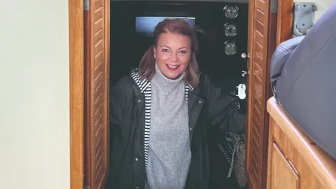 Mirjana Hrga nasmijana na brodu u sivoj dolčeviti i tamnoj jakni.