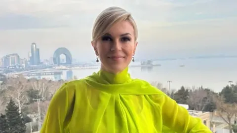 Kolinda Grabar-Kitarović u limeta zelenoj bluzi ispred vizure modernog grada.