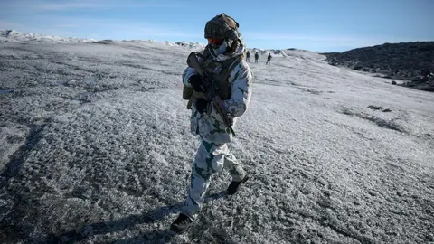 Vojnik u zimskoj amfibijskoj uniformi hoda po ledu s jurišnom puškom u rukama.