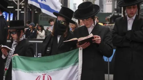 Pripadnici jevrejske zajednice u tradicionalnoj odjeći drže iransku zastavu i knjige.