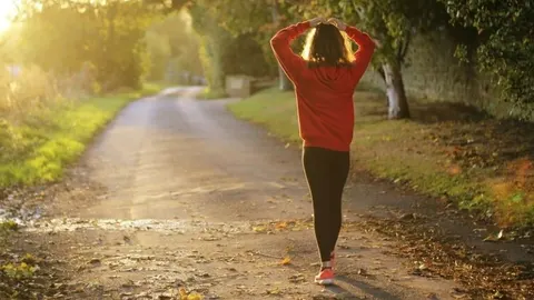 Žena u crvenoj majici hoda osvijetljenom stazom u prirodi