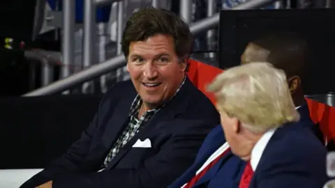 Tucker Carlson i Donald Trump sjede jedan pored drugoga na javnom događaju.