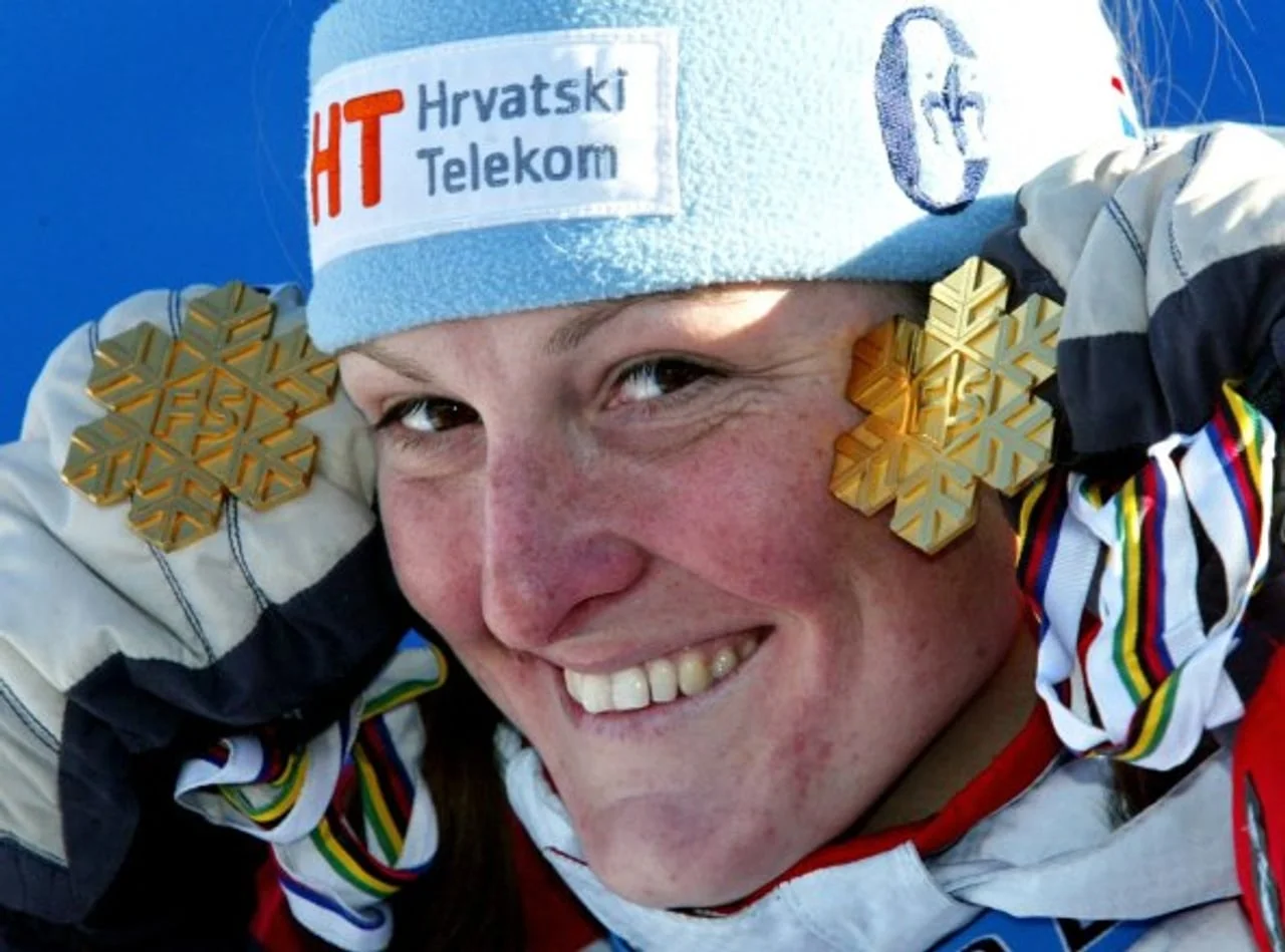 Nasmijana Janica Kostelić drži zlatne medalje u obliku pahuljica uz lice.